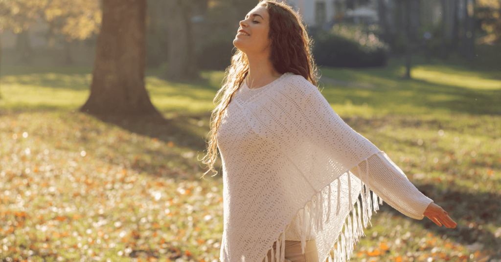 Imagem de uma mulher com os braços abertos e uma expressão de contentamento, paz e bem-estar, em meio ao ar livre. O rosto dela está inclinado para o alto, com os olhos fechados e um leve sorriso no rosto. Essa imagem busca representar a busca de uma pessoa pela paz do Senhor e o sentimento que ela possuí, quando encontra a paz do Senhor. Imagem destacada do site louvare.com, referente ao post: Descubra como experimentar a paz do Senhor de verdade: 7 passos simples para uma vida plena e feliz.