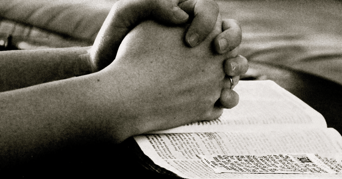 Imagem com duas mãos juntas em posição de oração, em cima de uma bíblia aberta. Imagem destacada do site louvare.com, referente ao post: Oração Poderosa: Encontrando Paz, Perdão e Sabedoria em Deus.