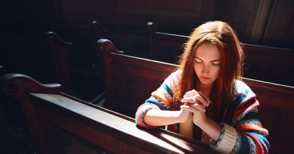 Imagem de uma mulher ajoelhada em um banco de igreja, com as duas mãos juntas em posição de oração a Deus, com os olhos fechados e uma expressão de meditação, oração e louvor a Deus. Imagem destacada do site louvare.com, referente ao post: Deus odeia o orgulho: Entenda a humildade que agrada a Deus